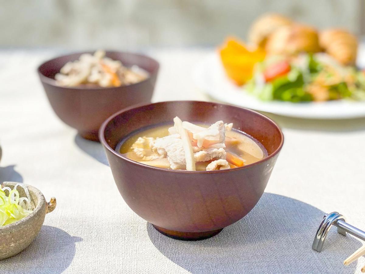 神戸メリケンパークオリエンタルホテル 神戸市 エクステリア 写真 The photo features a wooden bowl filled with a warm soup containing pieces of meat and vegetables. There are also two additional bowls in the background, along with a plate of salad and baked goods, suggesting a meal setting. The table is covered wit