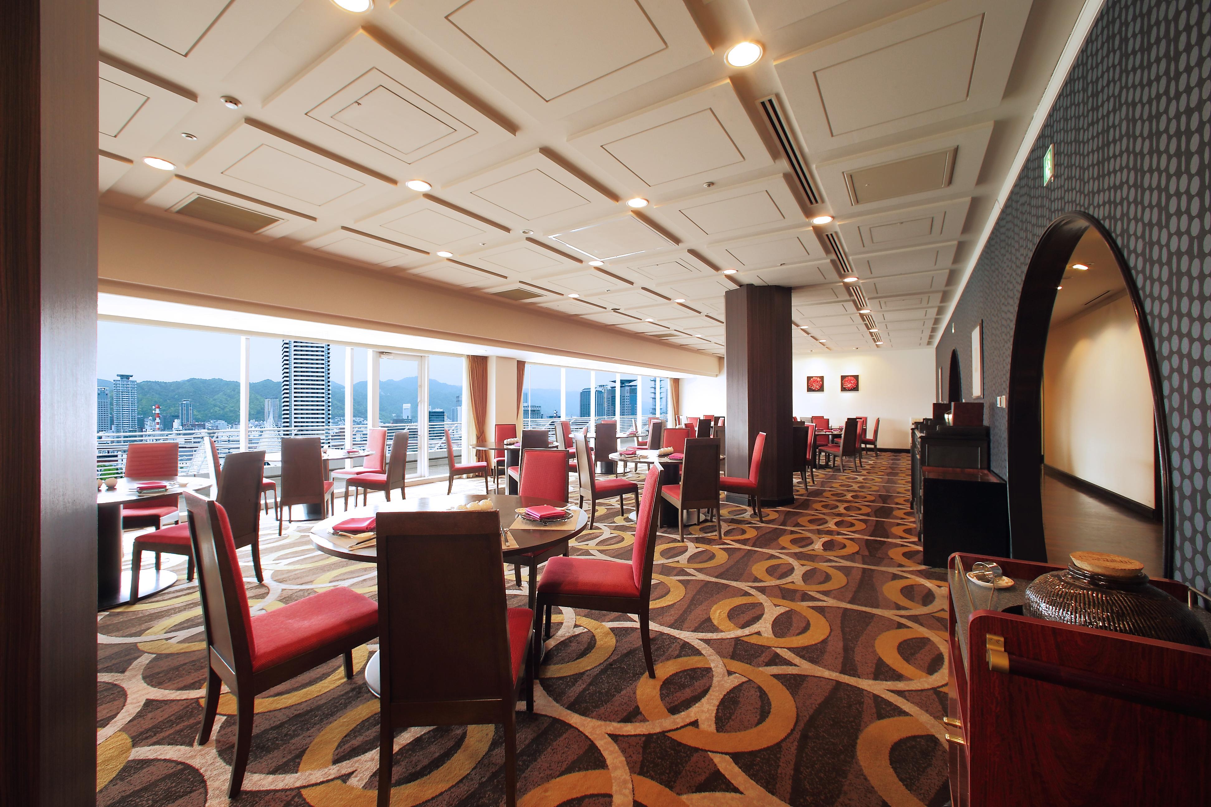 神戸メリケンパークオリエンタルホテル 神戸市 エクステリア 写真 The photo shows a modern restaurant interior with a stylish design. There are several tables and pairs of chairs arranged throughout the space, with a focus on red accents in the seating. The large windows provide a panoramic view of the outside envi