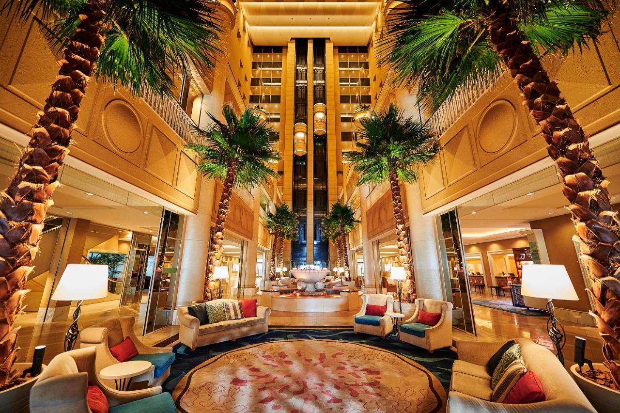 神戸メリケンパークオリエンタルホテル 神戸市 エクステリア 写真 The photo shows a luxurious hotel lobby featuring high ceilings and a spacious layout. There are tall palm trees strategically placed throughout the area, adding a tropical feel. Elegant seating arrangements, including plush armchairs and sofas in va