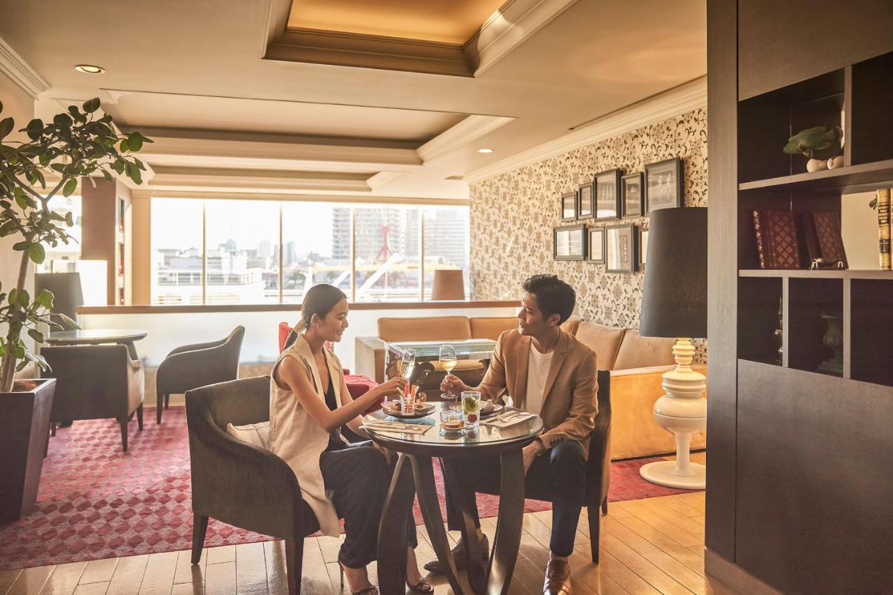 神戸メリケンパークオリエンタルホテル 神戸市 エクステリア 写真 The photo shows a cozy indoor setting, likely a cafe or restaurant, with two people seated at a small round table. They appear to be enjoying a meal or drinks together, with food and glasses in front of them. The interior features large windows letti