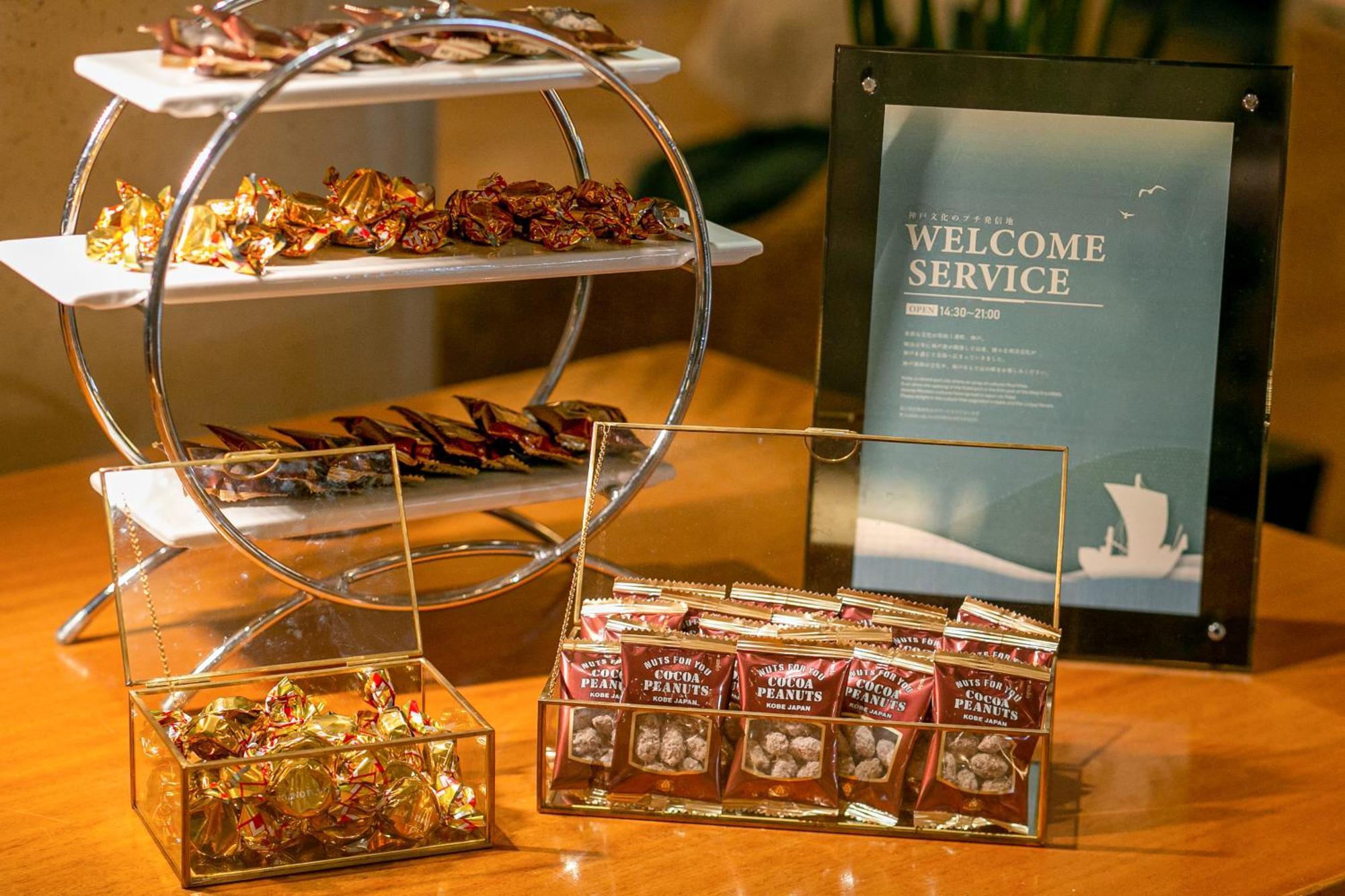 神戸メリケンパークオリエンタルホテル 神戸市 エクステリア 写真 The photo displays a welcome service setup featuring various treats. 

1. **Display Stand**: There is a tiered circular stand with an assortment of wrapped candies or chocolates on the upper and lower levels.

2. **Glass Container**: In front, there'