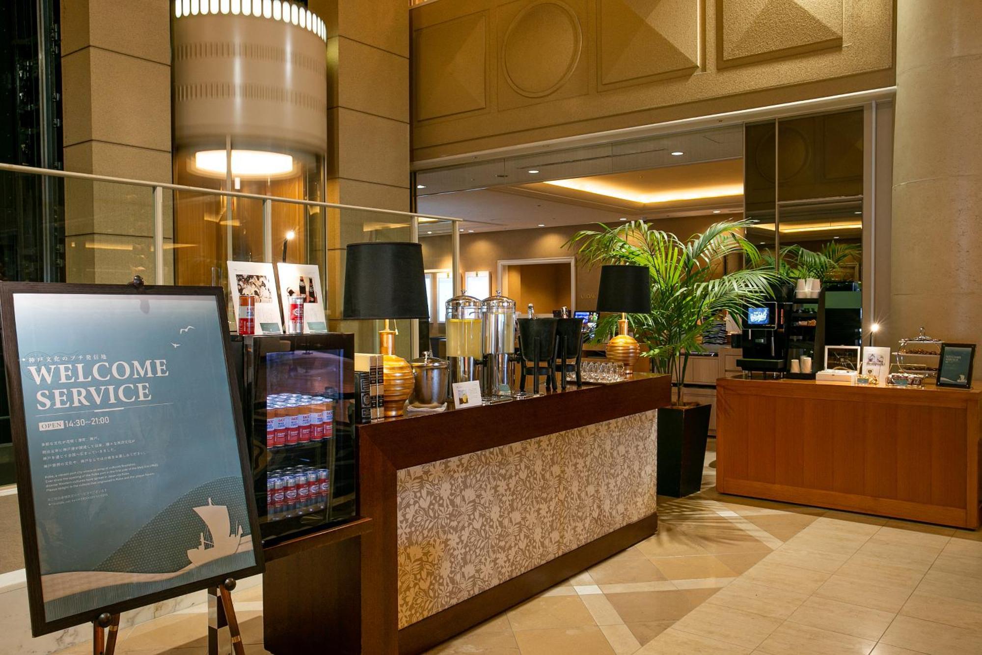 神戸メリケンパークオリエンタルホテル 神戸市 エクステリア 写真 The photo depicts an elegant reception area, likely in a hotel. There is a large sign that reads "WELCOME SERVICE" positioned prominently on the left. 

The reception desk is well-organized, featuring decorative elements like lamps and a beverage are