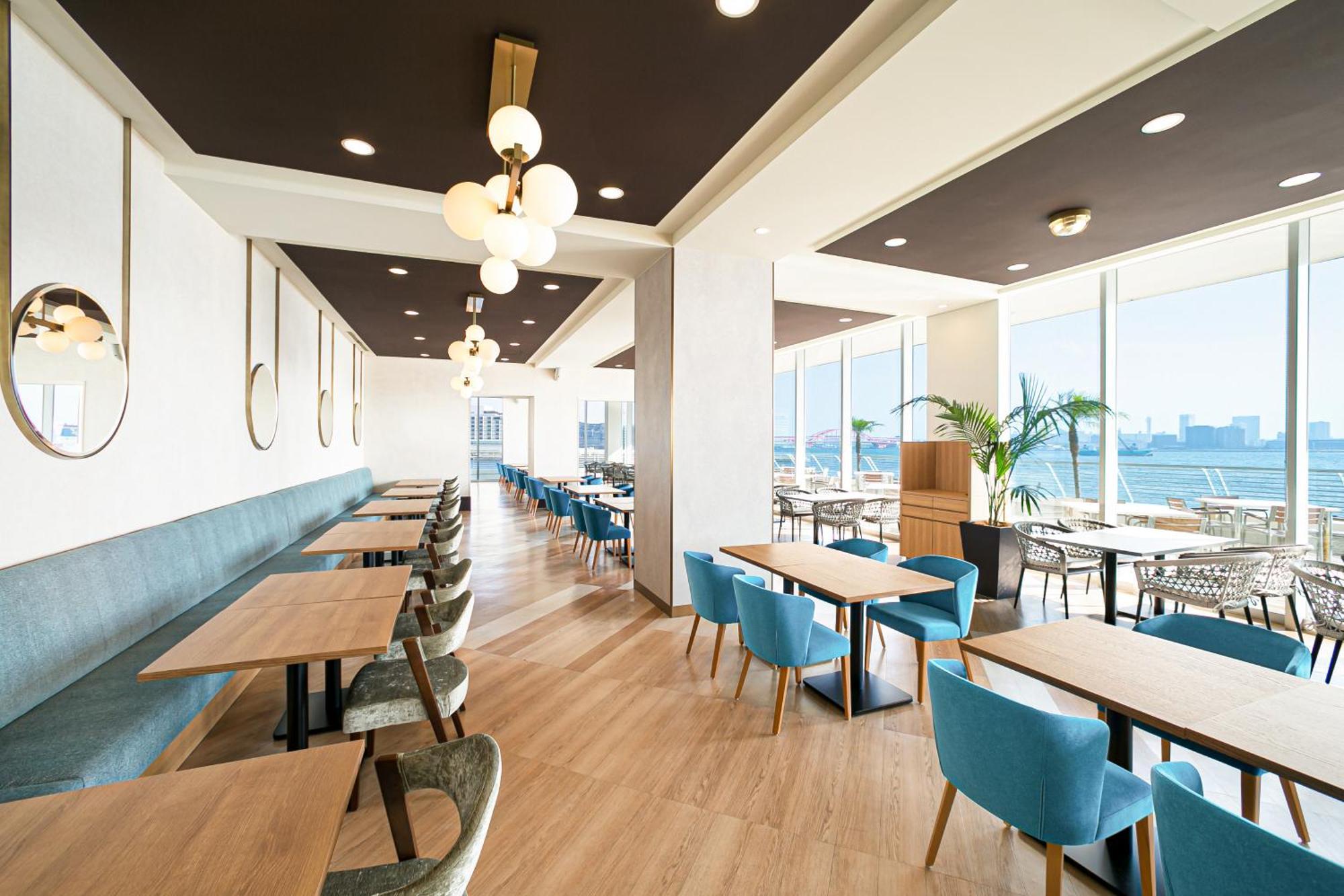 神戸メリケンパークオリエンタルホテル 神戸市 エクステリア 写真 The photo shows the interior of a modern restaurant or café, featuring a spacious and bright atmosphere. The design includes large windows that provide a view of the outside, allowing natural light to fill the space. There are various tables made of 