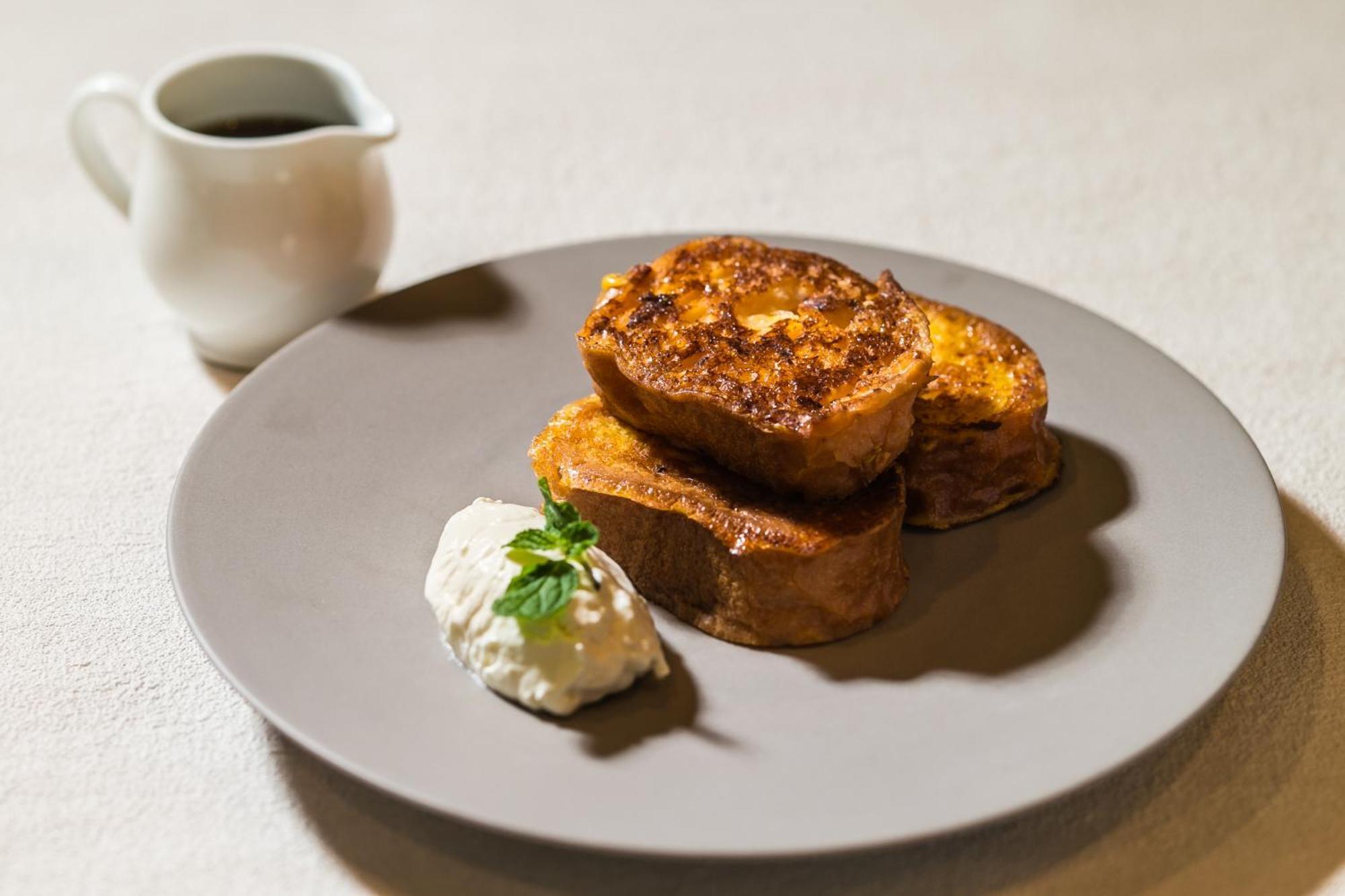 神戸メリケンパークオリエンタルホテル 神戸市 エクステリア 写真 The photo displays a plate of French toast, featuring several thick slices that are golden-brown and slightly crispy on the outside. Accompanying the toast is a dollop of whipped cream or a similar creamy topping, garnished with a small sprig of fres