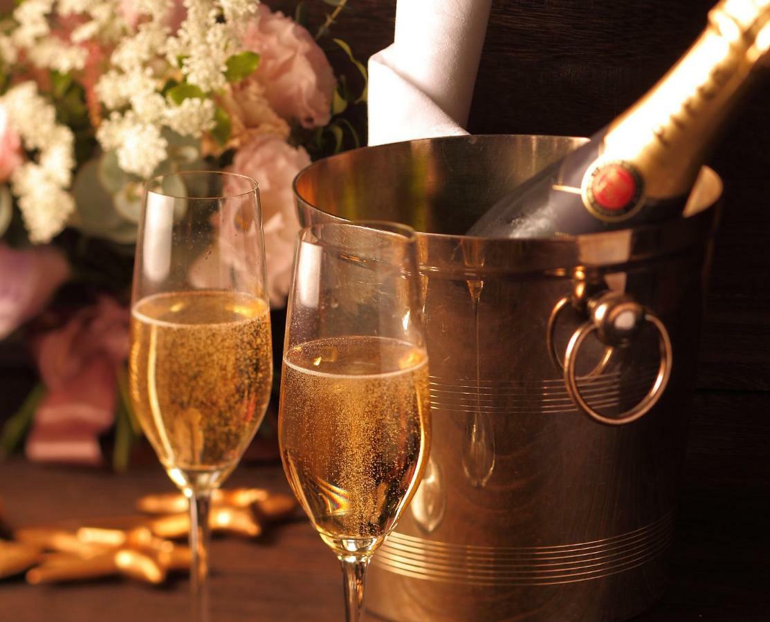 神戸メリケンパークオリエンタルホテル 神戸市 エクステリア 写真 The photo features two glasses of sparkling wine or champagne, filled with bubbly, golden liquid. Beside the glasses is a shiny metal ice bucket, which contains a bottle of champagne that has been placed inside. In the background, there are delicate 
